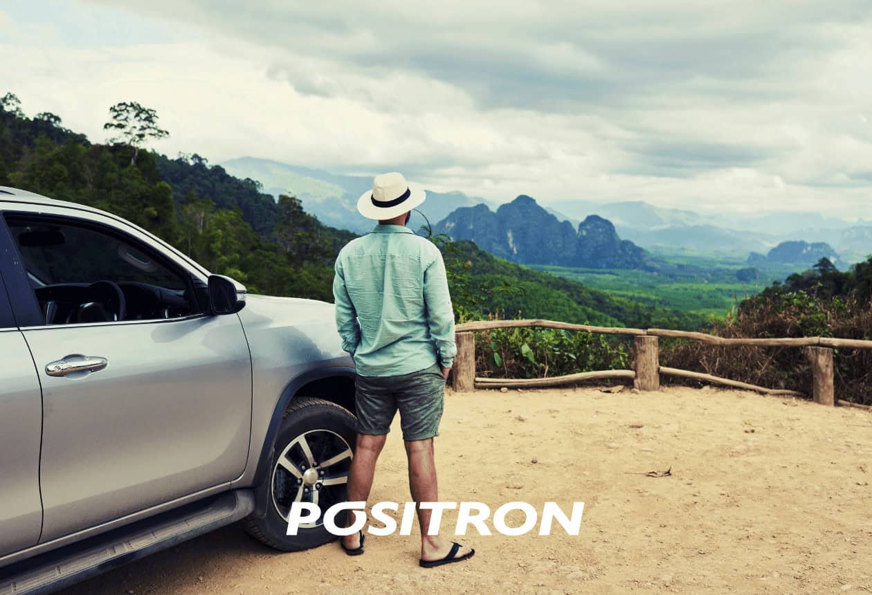 homem de costas com chapéu ao lado de um carro olhando a paisagem ao fundo